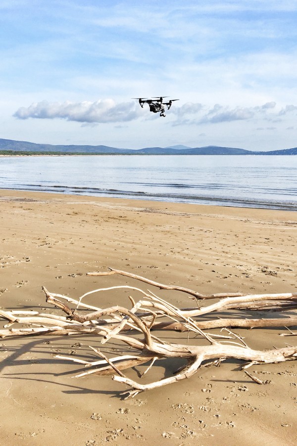 drone dji inspire 1 su spiaggia con tronco di albero e mare sullo sfondo